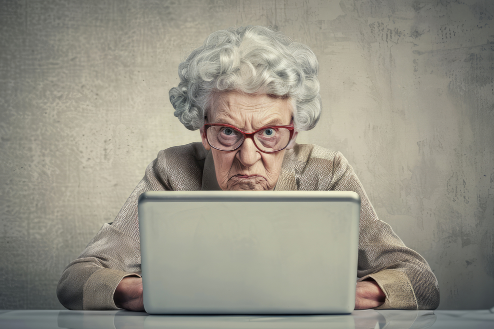 Ältere Frau sitzt wütend vor Laptop.